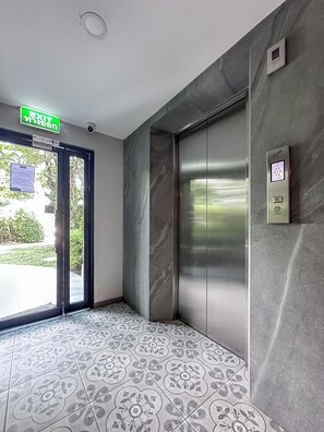 An elevator with a control panel, a door with an exit sign, and patterned floor tiles. - The Title Residencies Naiyang Beach Apartment G507 (Thalang/Sakhu)