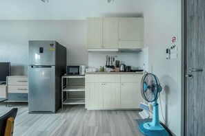 Eine kleine Küche mit Kühlschrank, Mikrowelle und einem blauen Ventilator.