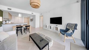 Uma sala de estar moderna com um sofá, uma mesa de centro, uma televisão e um espaço de jantar com cadeiras e uma mesa.