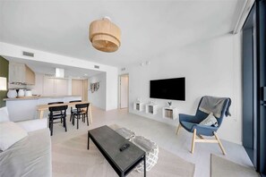 A modern living room with a sofa, a coffee table, a TV, and a dining area with chairs and a table. - Brickell Skyline with Rooftop Pool & Spa (Miami)