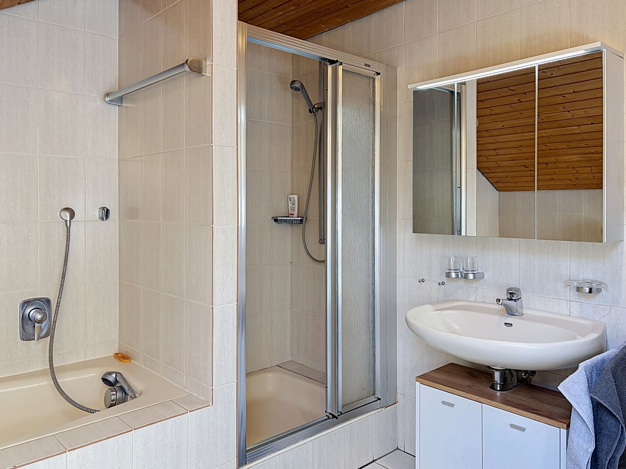 A modern bathroom with a glass-enclosed shower, a white sink, and a wooden ceiling.