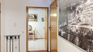 A hallway with a tiled floor, a glass-top table, a door leading to a room, and a framed black and white photograph on the wall. - Vacation home JANIKE by Interhome (Regensburg)