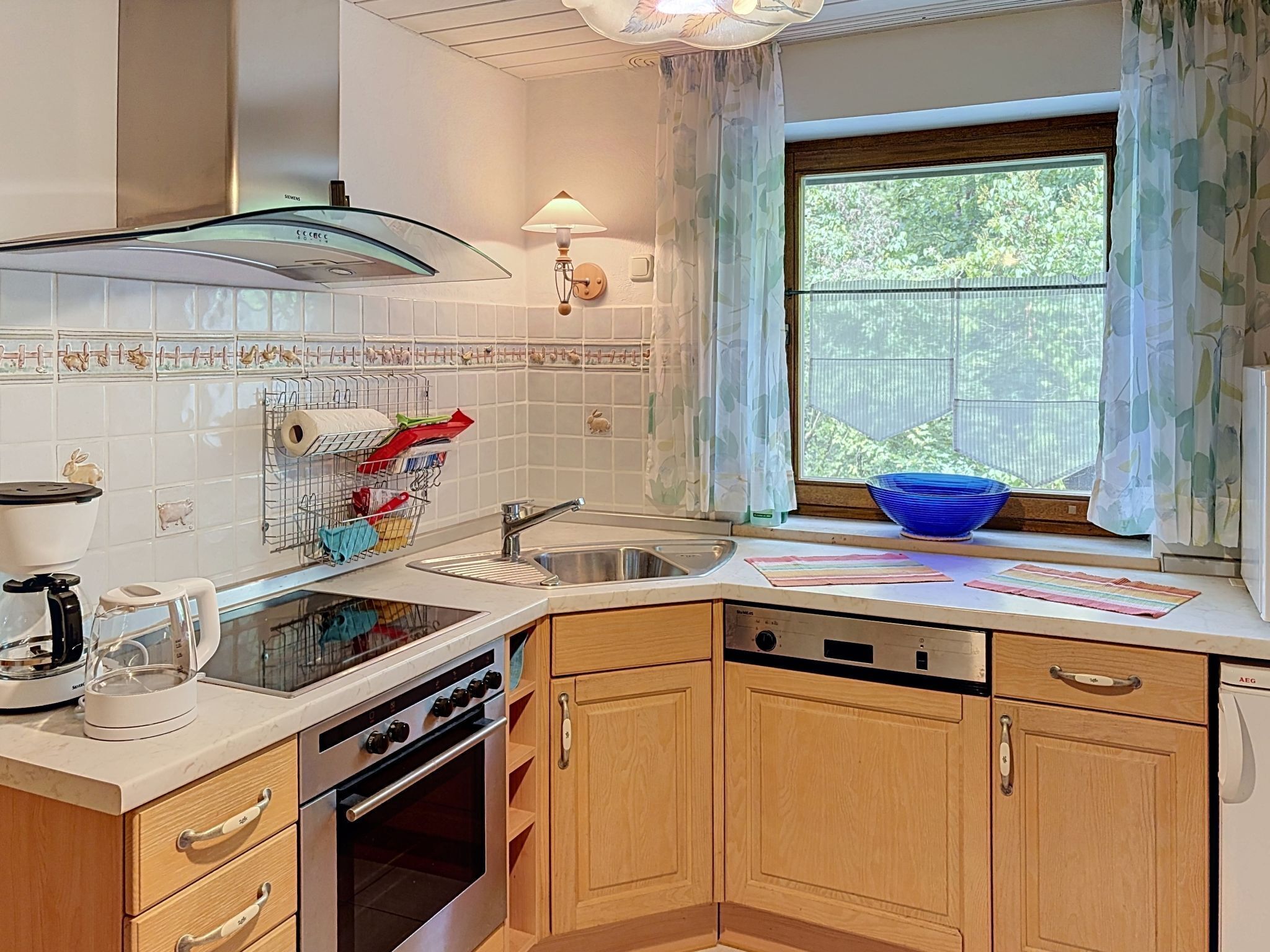 A kitchen with a stove, sink, and a window with a view of greenery.