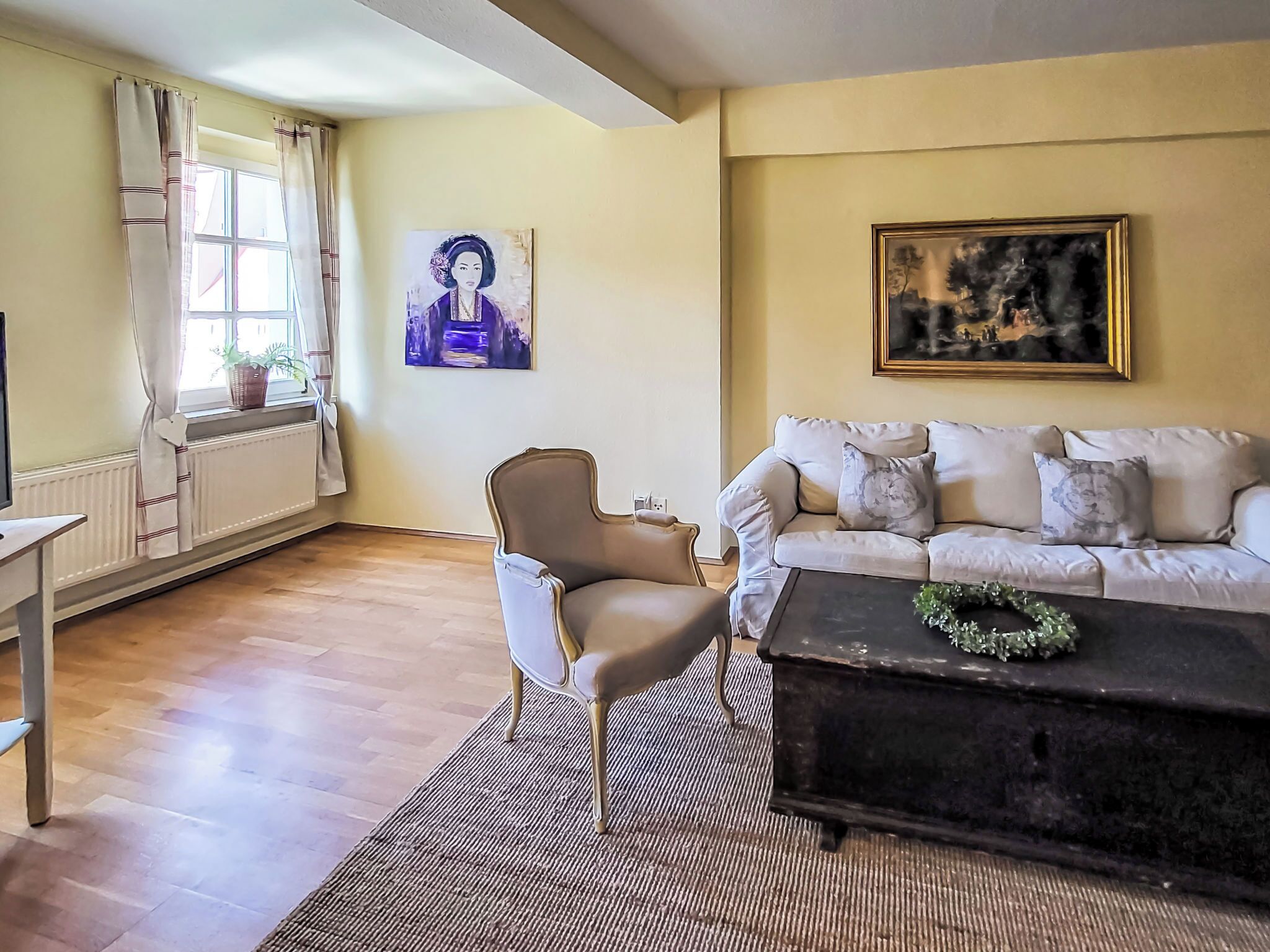 Een woonkamer met een bank, een fauteuil, een salontafel en een schilderij aan de muur.