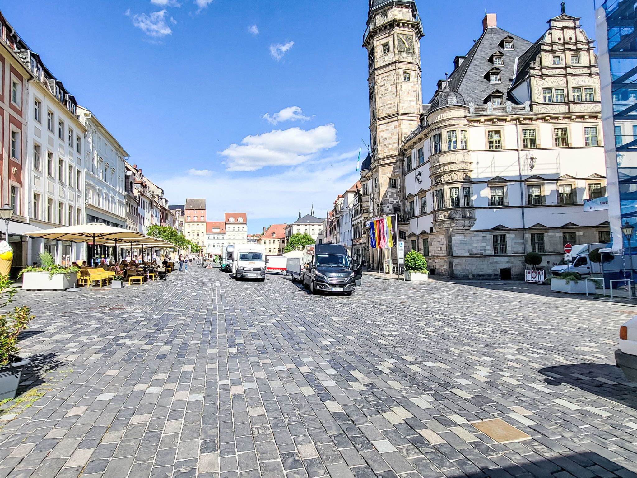 A cobblestone street lined with historic buildings, a clock tower, and a clear blue sky.
