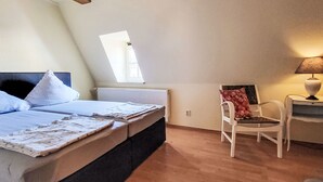 Un dormitorio con cama, una silla, una mesa, un ventanal y un radiador.