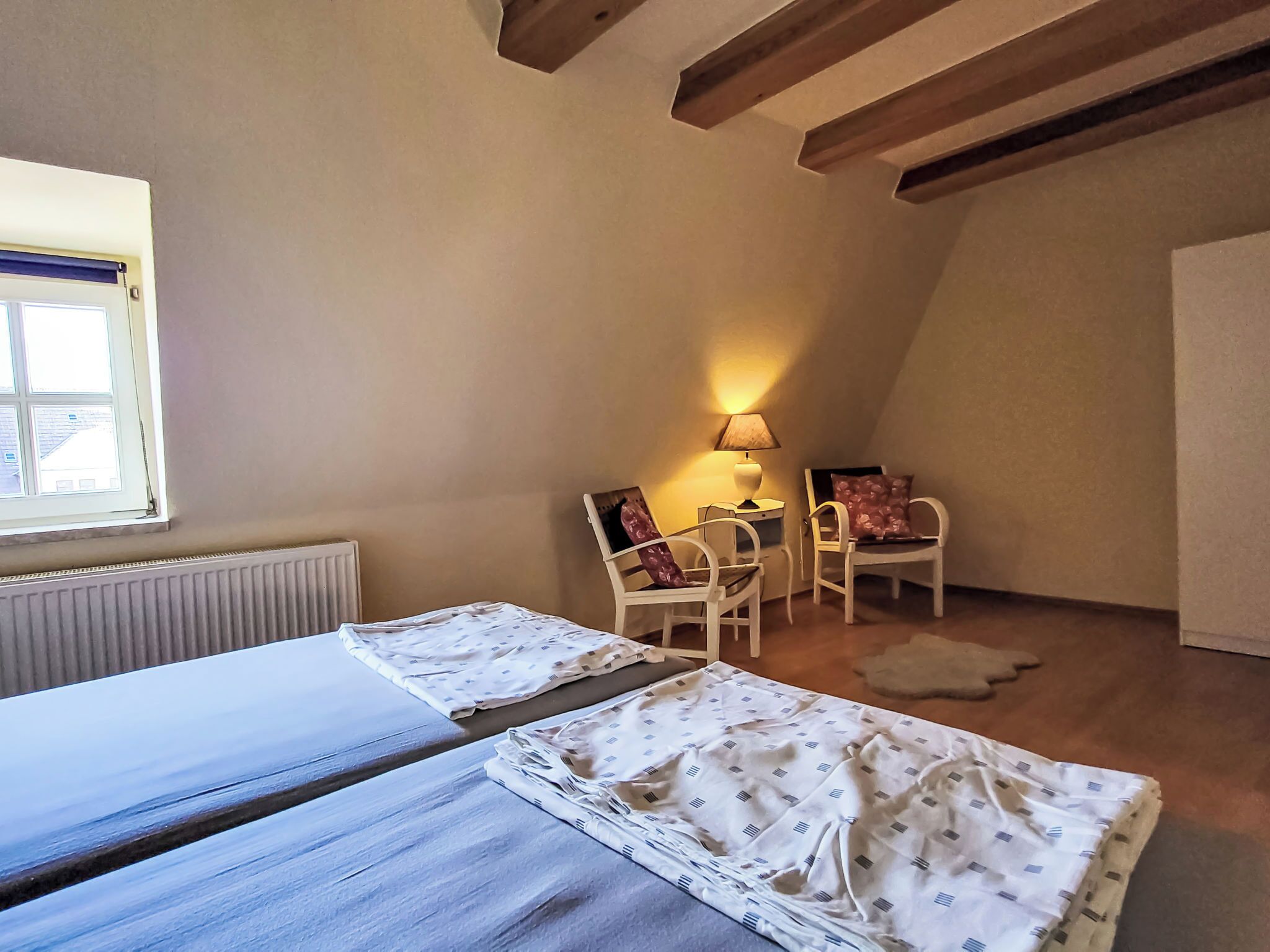 Une chambre avec deux lits, une fenêtre, un radiateur, une lampe et une chaise.