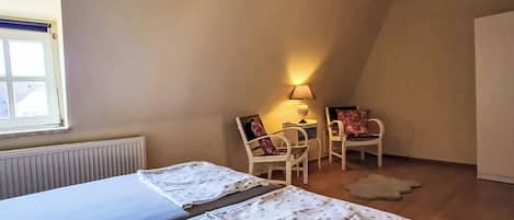 A room with two beds, a window, a radiator, a lamp, and a chair.