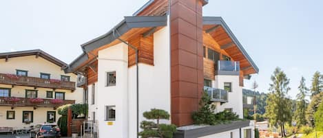 A modern building with a sloped roof, a stone base, and a small garden area with plants and a tree.