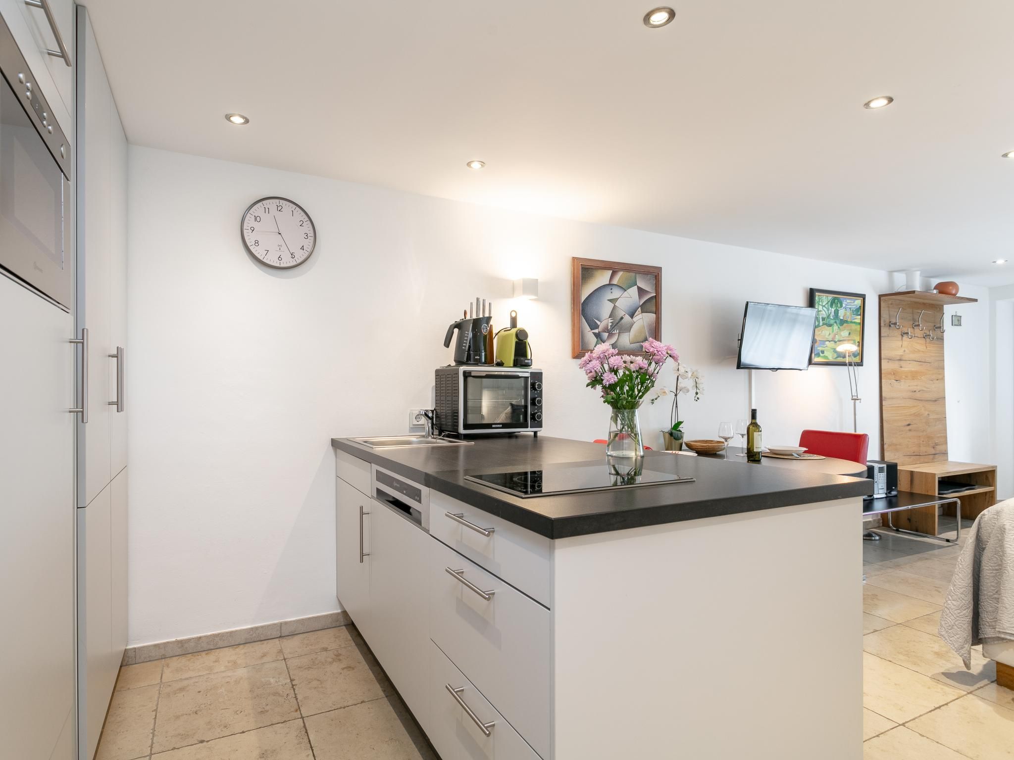 Een moderne keuken met een centraal eiland, inbouwapparatuur en een klok aan de muur.