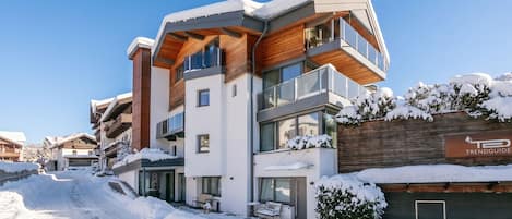 A modern multi-story building with balconies, a garage, and a snow-covered landscape.