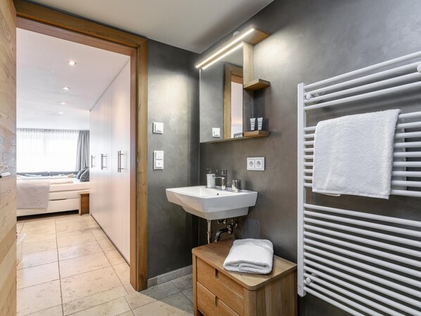 A modern bathroom with a sink, mirror, towel rack, and a wooden stool.