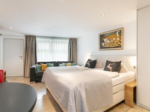Ein modernes Schlafzimmer mit einem großen Bett, einer Couch, einem Esstisch und einem Gemälde an der Wand.