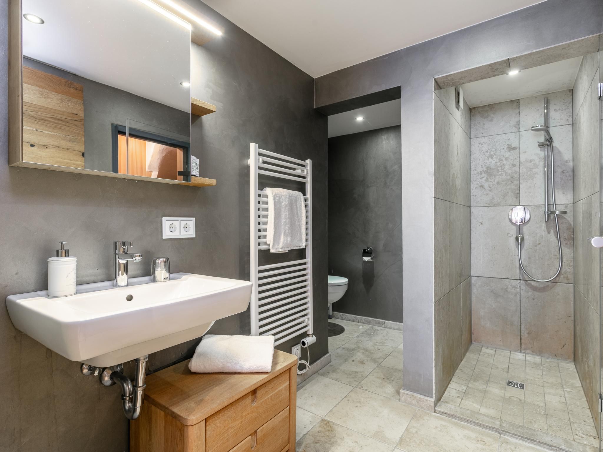Een moderne badkamer met een witte wasbak, houten wastafelmeubel, een handdoekrek, een spiegel, een douche en een toilet.