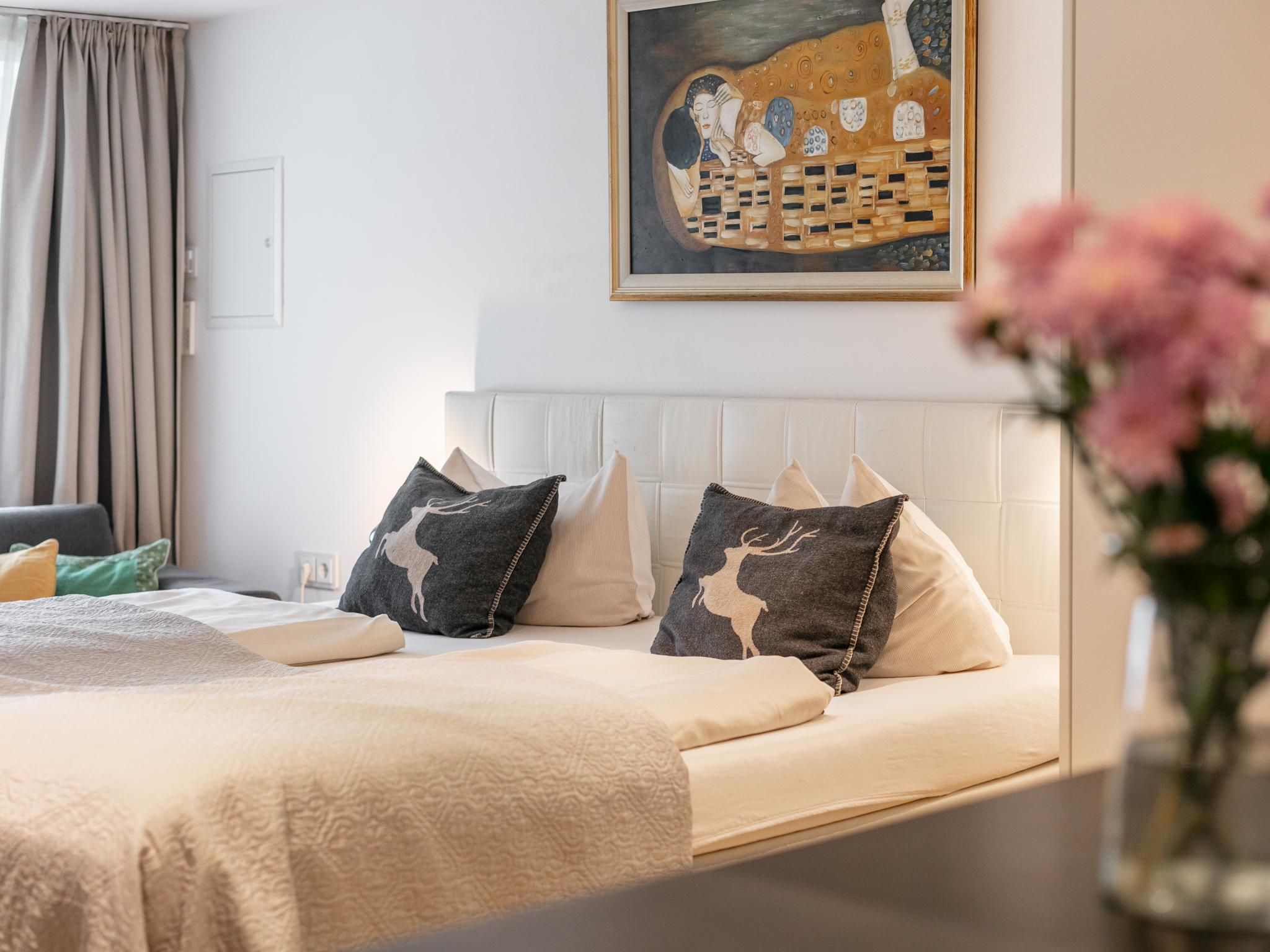 A hotel room with a bed, pillows, a painting, and a vase with flowers.
