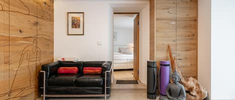 A modern living room with a black leather sofa, a wooden wall with a map, a framed picture, and a meditation statue.