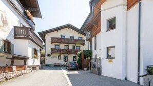 Eine enge Straße mit einem Gebäude mit Balkonen und Blumenkästen, einem davor geparkten Auto und blauem Himmel.
