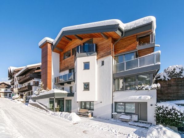A modern multi-story building with a wooden facade, large windows, and a snow-covered roof.