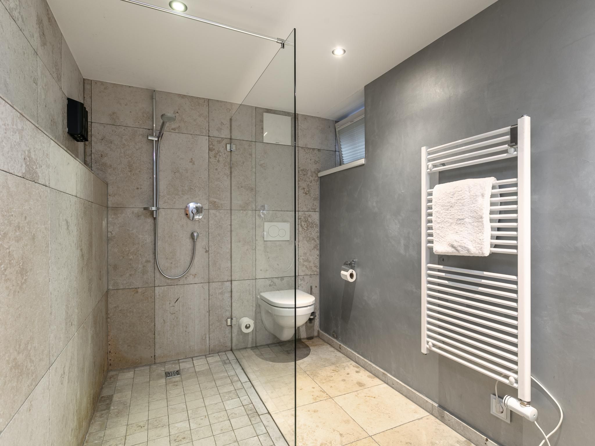 Een moderne badkamer met een douchecabine van glas, een toilet en een handdoekhouder.