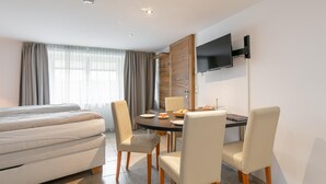 Ein Hotelzimmer mit einem Bett, einem Esstisch mit Stühlen, einem flachbildfernseher an der Wand und einem Fenster mit Vorhängen.