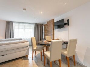 Ein Hotelzimmer mit einem Bett, einem Esstisch mit Stühlen, einem flachbildfernseher an der Wand und einem Fenster mit Vorhängen.
