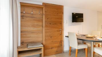 Une chambre moderne avec une armoire en bois, un banc, une table à manger avec des chaises et un téléviseur à écran plat fixé au mur.