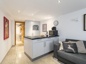 A modern kitchen with a built-in oven, microwave, and sink. There is a dining area with a grey sofa and a decorative pillow.