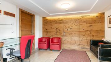Een modern receptiegebied met een houten wandpaneel, een glazen toonbank, rode stoelen, een zwarte leren bank en een rode vloerkleed.