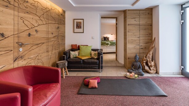 Ein modernes Wohnzimmer mit einem roten Ledersofa, einem schwarzen Leder-Couch, einer Holzwand mit abstrakten Mustern, einer Meditationsmatte und einer Statue.