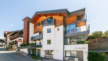 A modern multi-story building with balconies, large windows, and a mix of wooden and white exterior materials.
