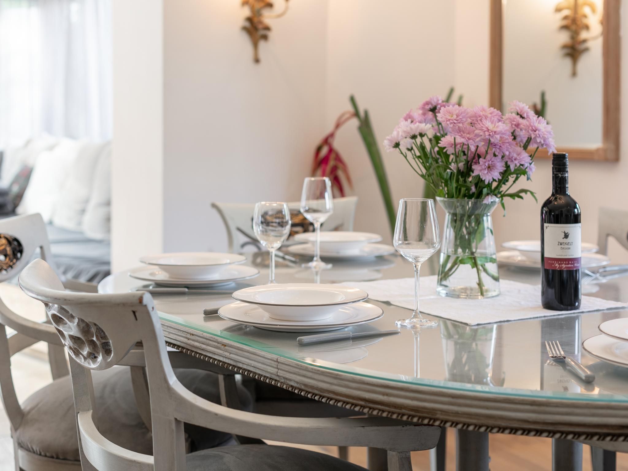 Une table à manger dressée avec des assiettes, des verres et une bouteille de vin, entourée de chaises.