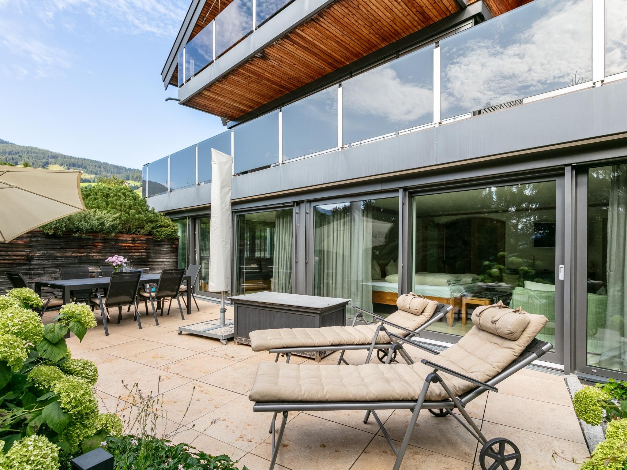 A modern outdoor patio with lounge chairs, a table, and a wooden deck.