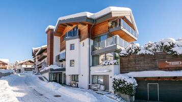 Een modern, meerhoog gebouw met een met sneeuw bedekte kap en balkons, omgeven door een besneeerd landschap.