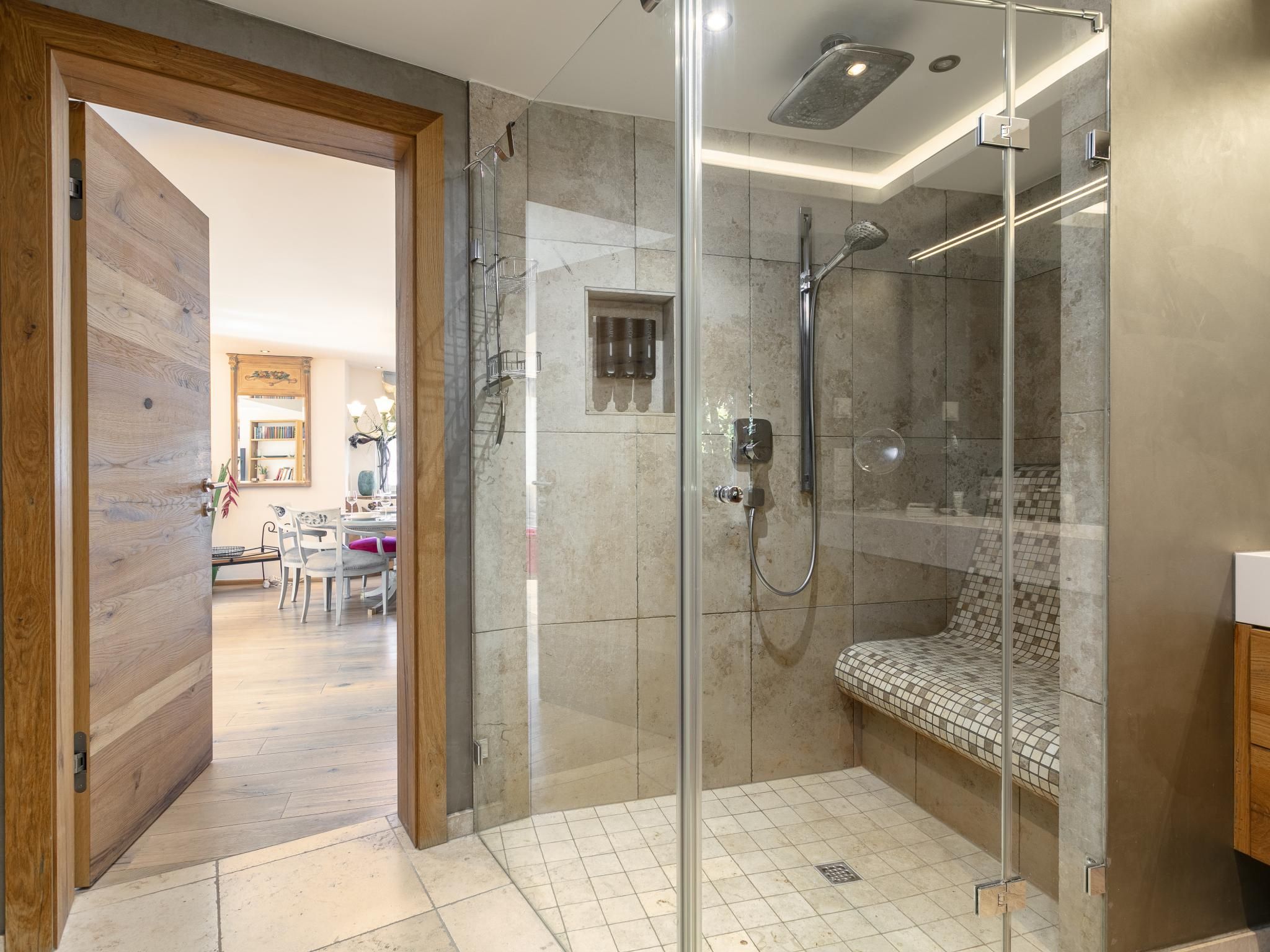 Een moderne badkamer met een glazen douchecabine, een bankje en een toilet.