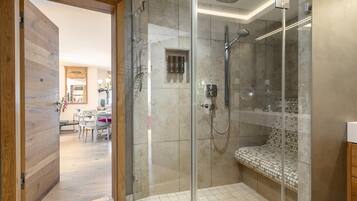 Een moderne badkamer met een glazen douchecabine, een bankje en een toilet.
