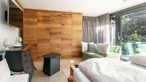 Ein modernes Schlafzimmer mit einem großen Bett, einer Couch, einem an der Wand montierten Fernseher und einem Fenster mit Vorhängen.