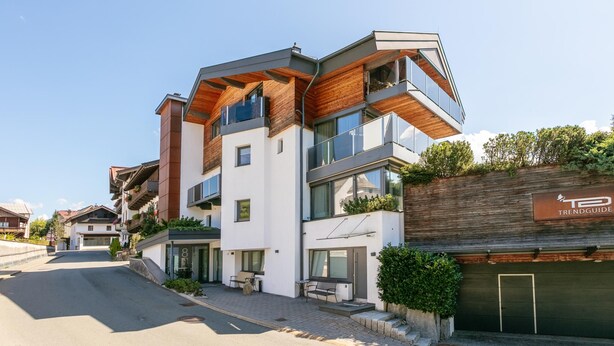 Ein modernes, mehrstöckiges Gebäude mit einer Kombination aus Holz- und Glasfassaden, einer sichtbaren Garage und wolkenlosem Himmel.