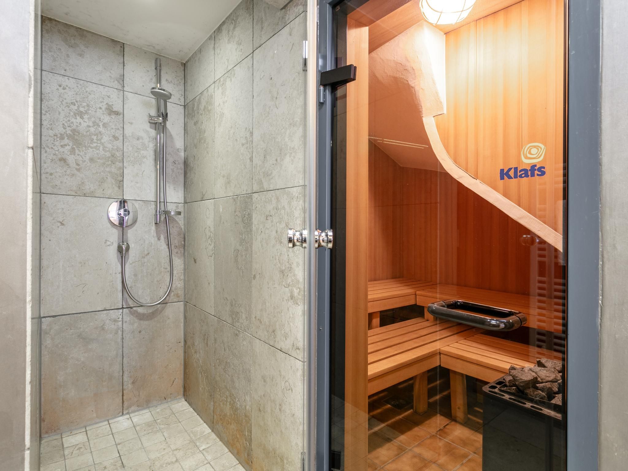 Un espace douche doté d’une porte en verre, un sauna en bois visible à travers la porte, et un logo sur la porte du sauna.