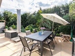 Un patio al aire libre con una mesa, sillas, una sombrilla y un jardín al fondo.