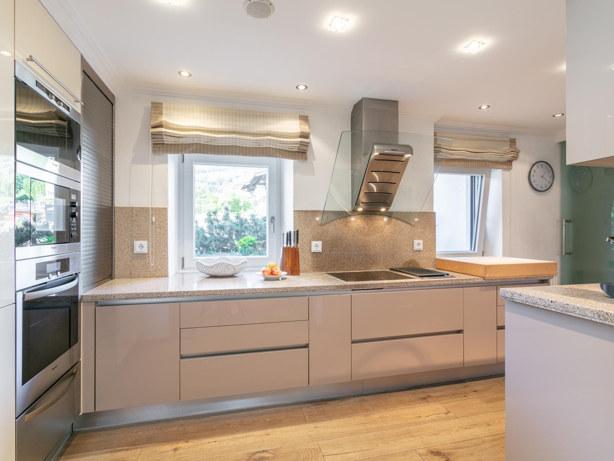 A modern kitchen with built-in appliances, a large window, and a view of greenery outside.