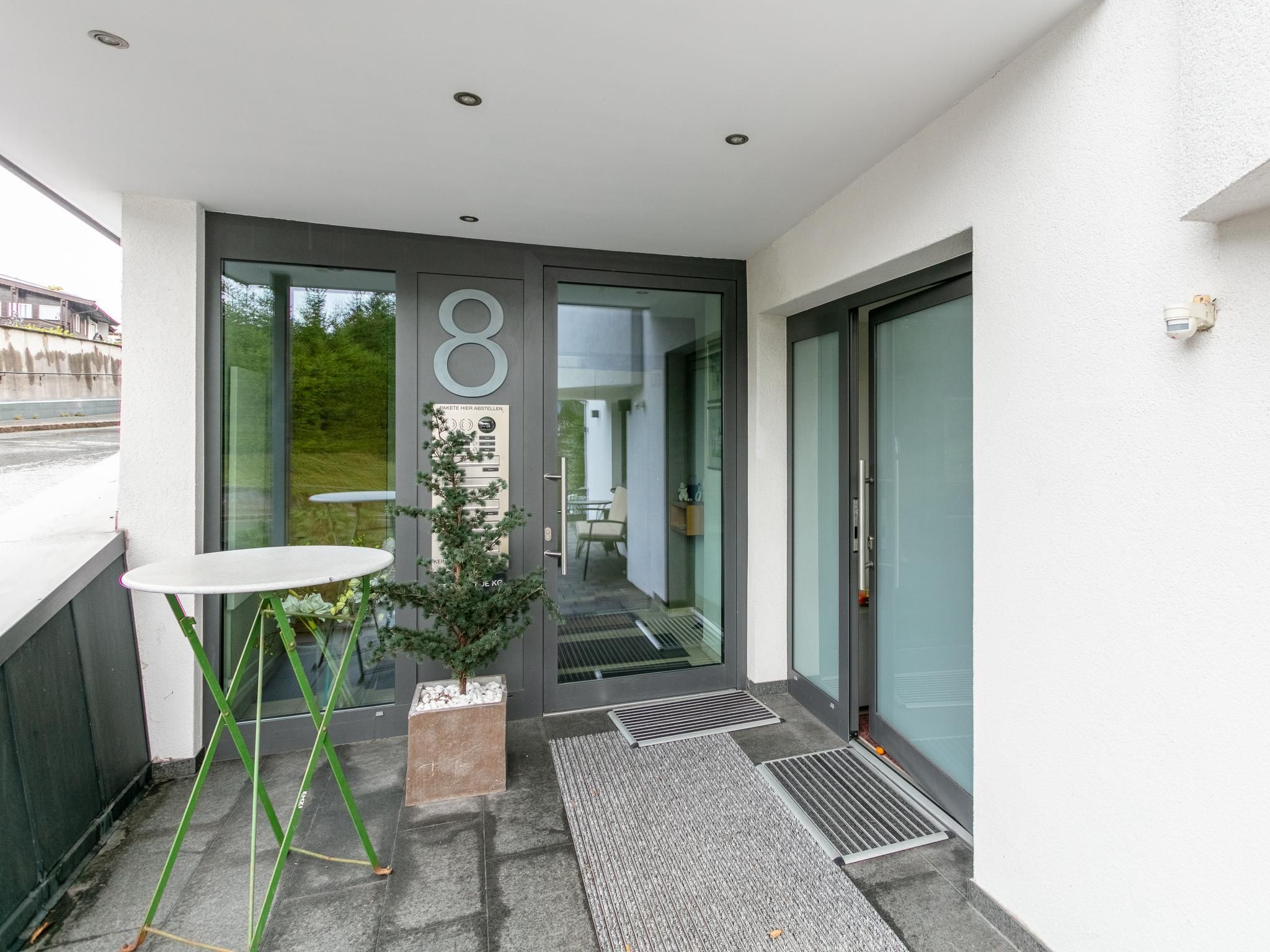 A modern entrance with a glass door, a small outdoor table, and a potted plant.
