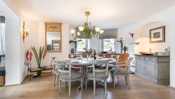 Een ruime eethoek met een ronde tafel en stoelen, een kroonluchter en een keuken op de achtergrond.