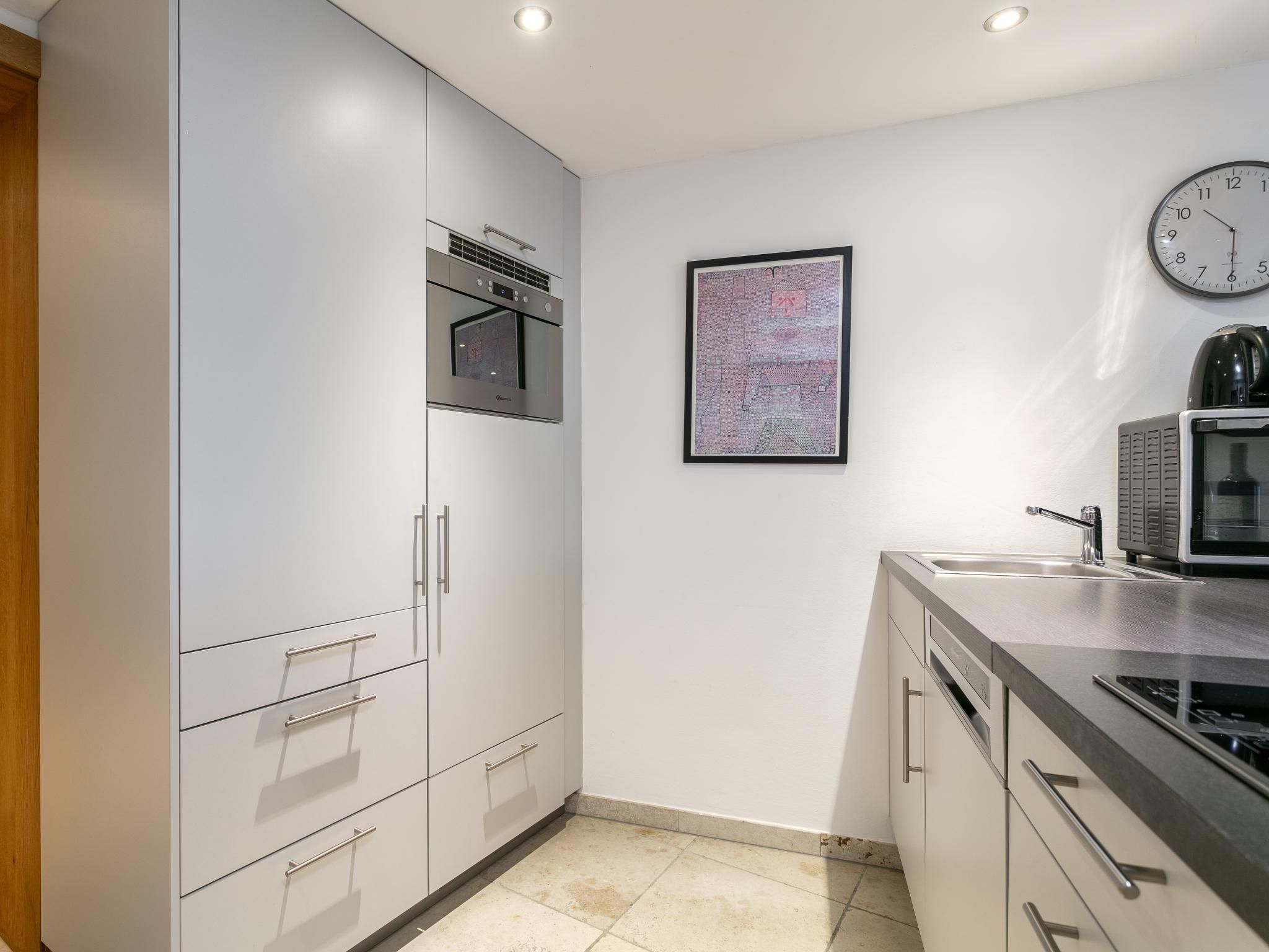 A modern kitchen with stainless steel appliances, a wall-mounted clock, and a framed artwork.