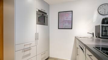 A modern kitchen with stainless steel appliances, a wall-mounted clock, and a framed artwork.