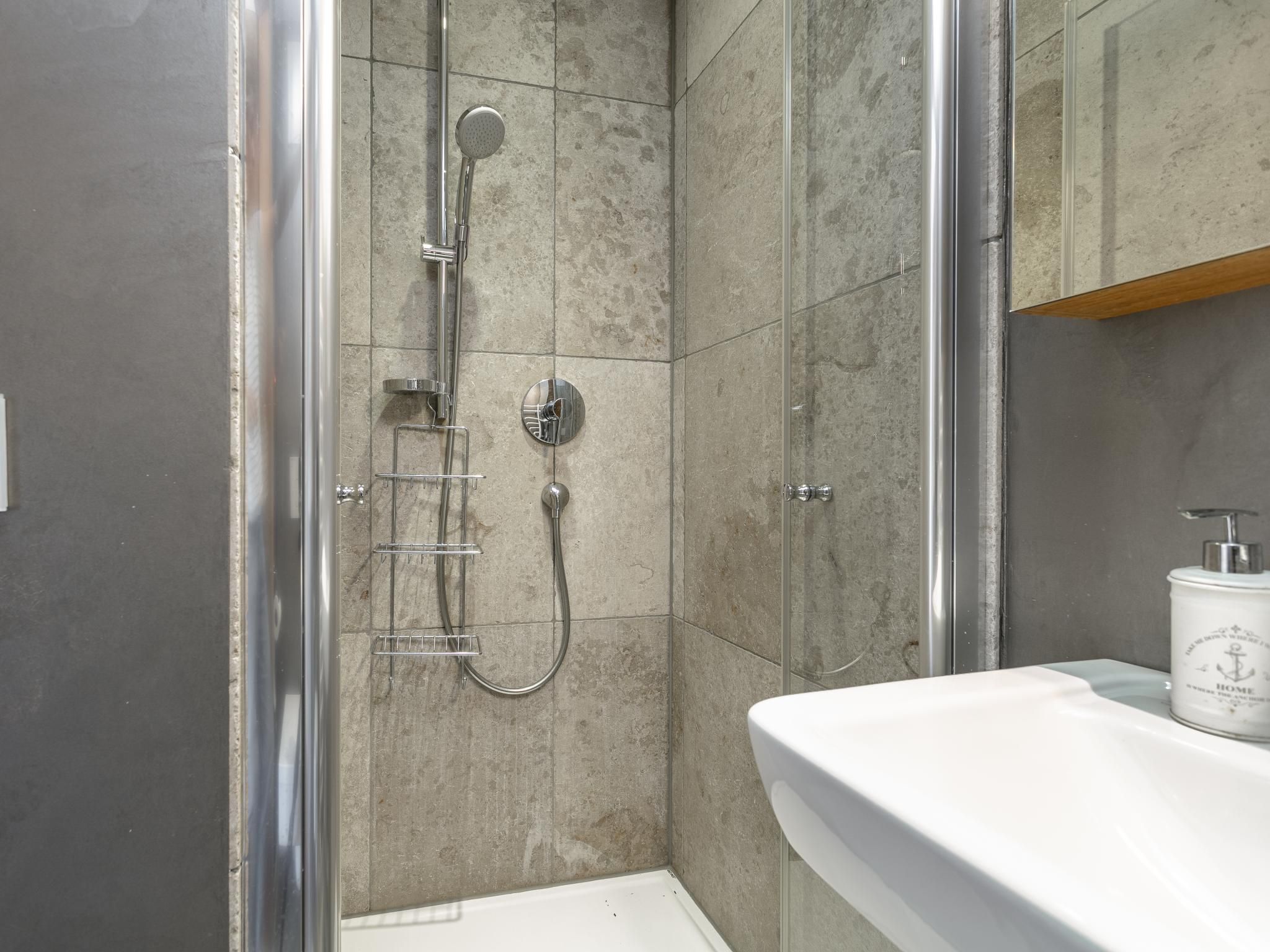 Een moderne badkamer met een douche met glazen wand, een wit wastafelmeubel en een douchewand betegeld met marmer.