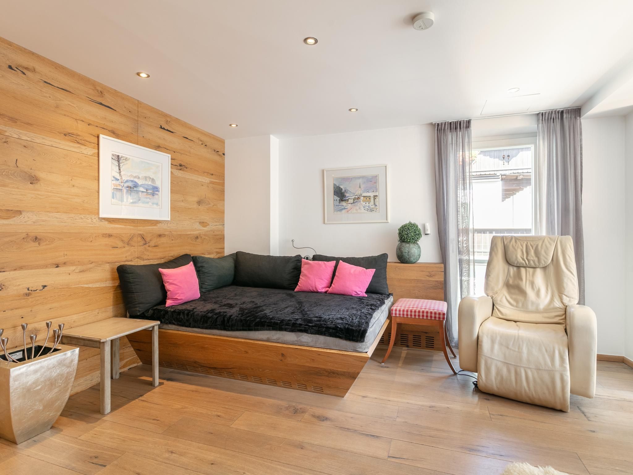 A modern bedroom with a wooden wall, a bed with black and pink bedding, a side table, a chair, and two framed artworks.