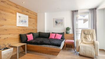 A modern bedroom with a wooden wall, a bed with black and pink bedding, a side table, a chair, and two framed artworks.