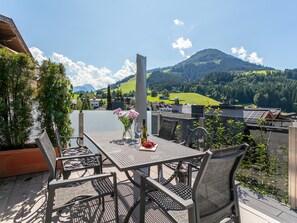 Terraza exterior con mesa lista para comer, rodeada de sillas y vista panorámica de un lago y montañas.
