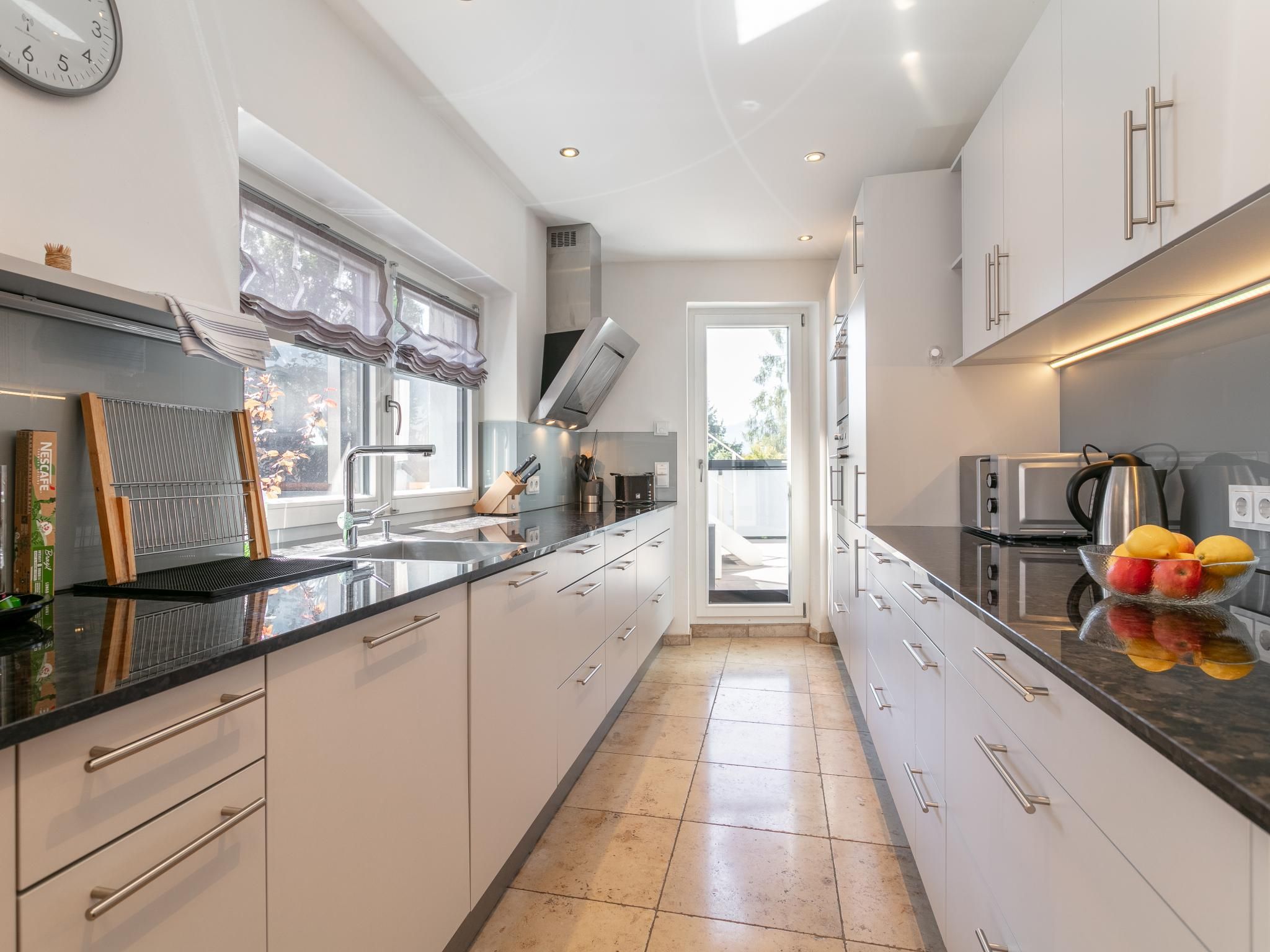 A modern kitchen with a central island, stainless steel appliances, and a view to the outside.