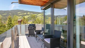 A balcony with a wooden deck, a glass door, wicker furniture, and a barbecue grill.